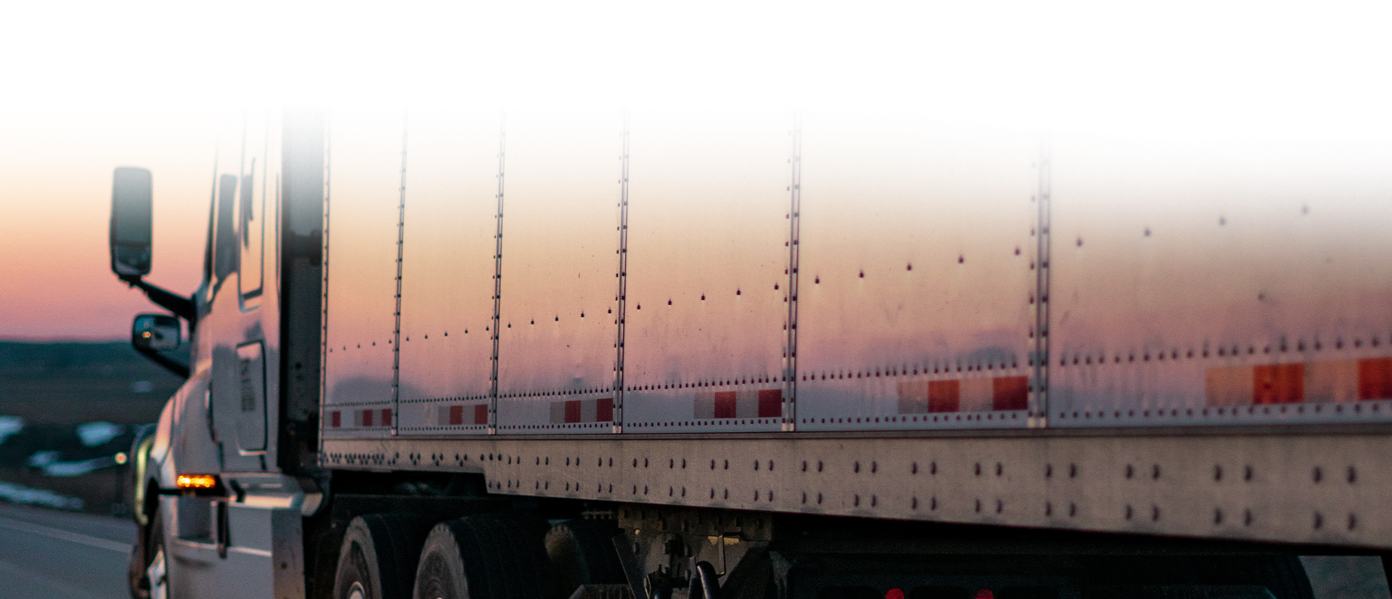 A large truck with the sun setting behind it.