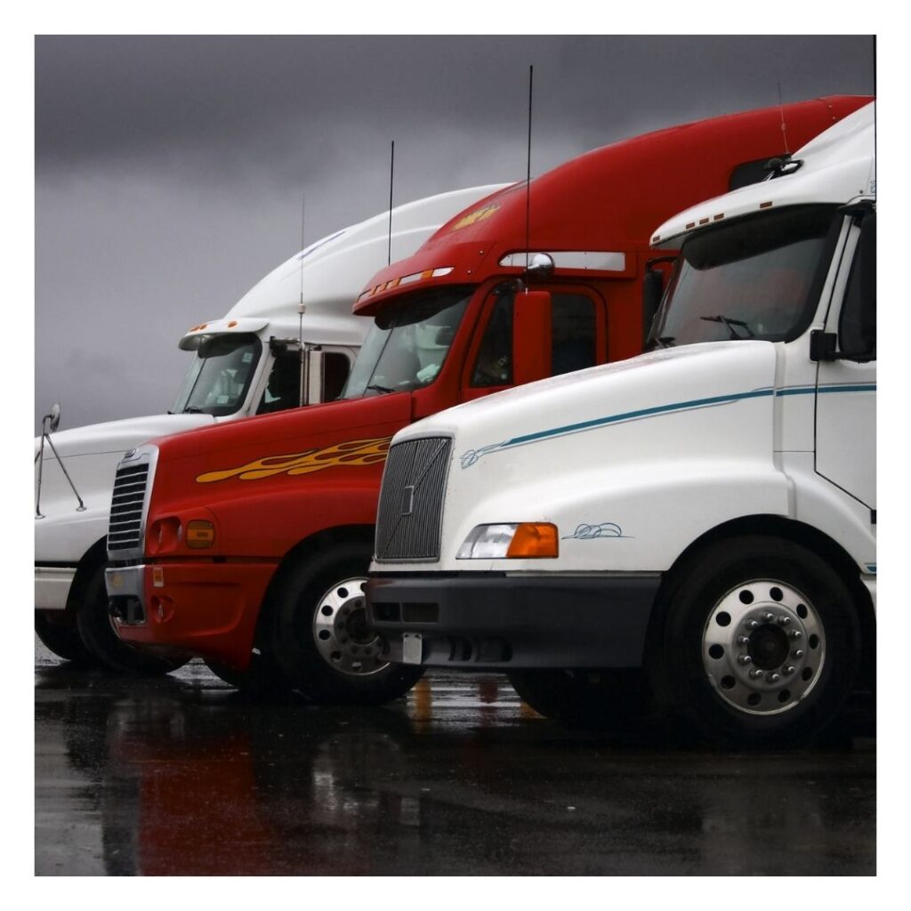 A row of semi trucks parked in the rain.