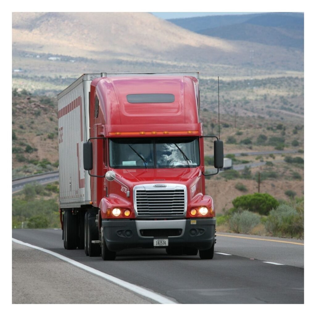 A red truck driving down the road near some mountains.