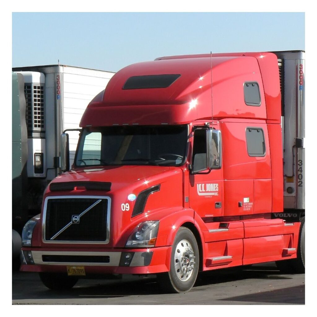 A red truck is parked next to two other trucks.