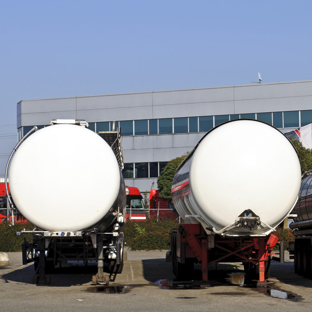 Two large white tanker trucks parked in a parking lot.